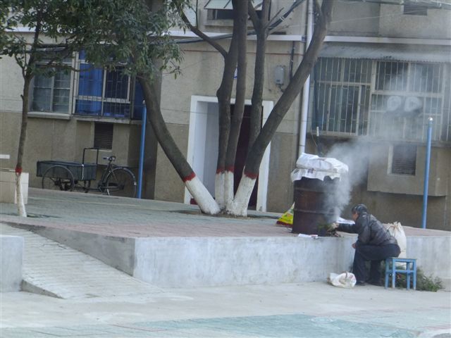 南阳网讯 (见习记者单衣上路)临近年底,市区居民都在准备年货,1月5日,记者发现,在市区小区内有人在自家门口熏制过年用的腊肉,如此做法污染了自己门口的空气,实在是得不偿失。 1月5日上午10点,记者从油田双河新苑小区路过,在小区32号楼附近,发现有浓烟冒起。记者在楼房附近发现,有人在用自制的熏炉熏制腊肉。记者看到,有几个居民蹲在油桶改造成的熏炉跟前,不停地往熏炉里填烧松枝柏桠。熏炉的上方,放着一条条猪肉,猪肉用报纸遮盖着,靠下面起的烟气熏烤。熏炉冒出来的烟气,不断地飘向空中,污染着洁净的空气